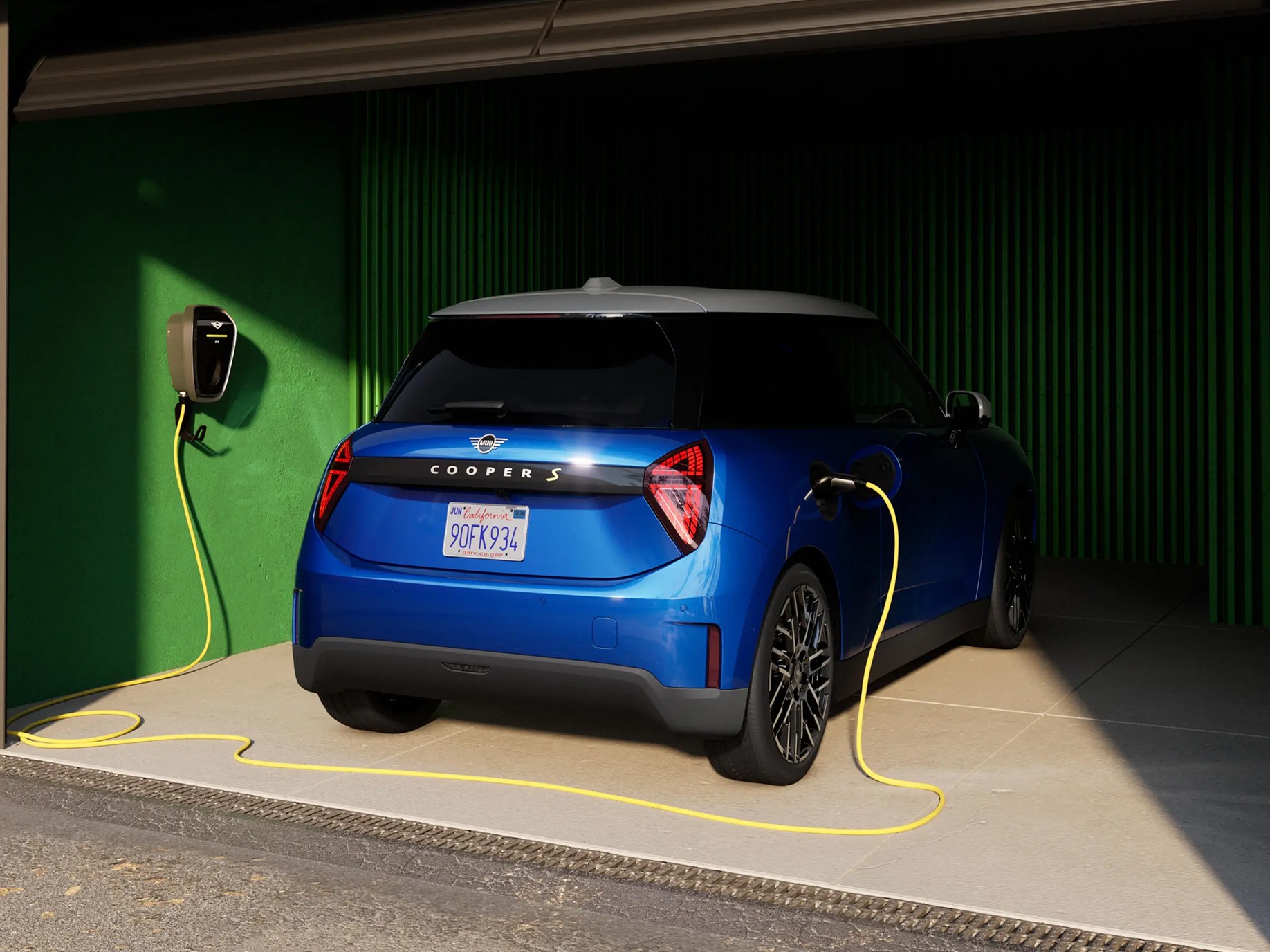 Rear view of Blazing Blue all-electric MINI Cooper in garage with charging cable